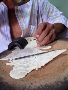 Detail of man chiseling the hide to create minutely detailed, symbolic pattern.