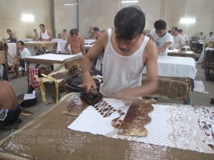 A man carefully uses a wax paper mask to create a curved edge to his cap printing